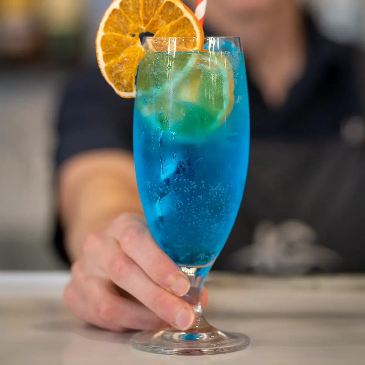 Server presenting a semi-transparent blue-coloured drink.