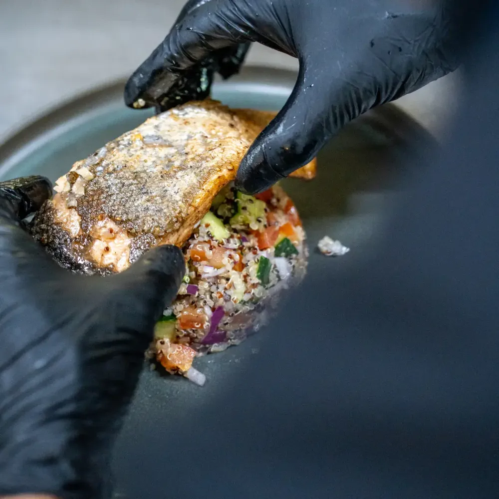 Server plating fish on top of quinoa on a plate.