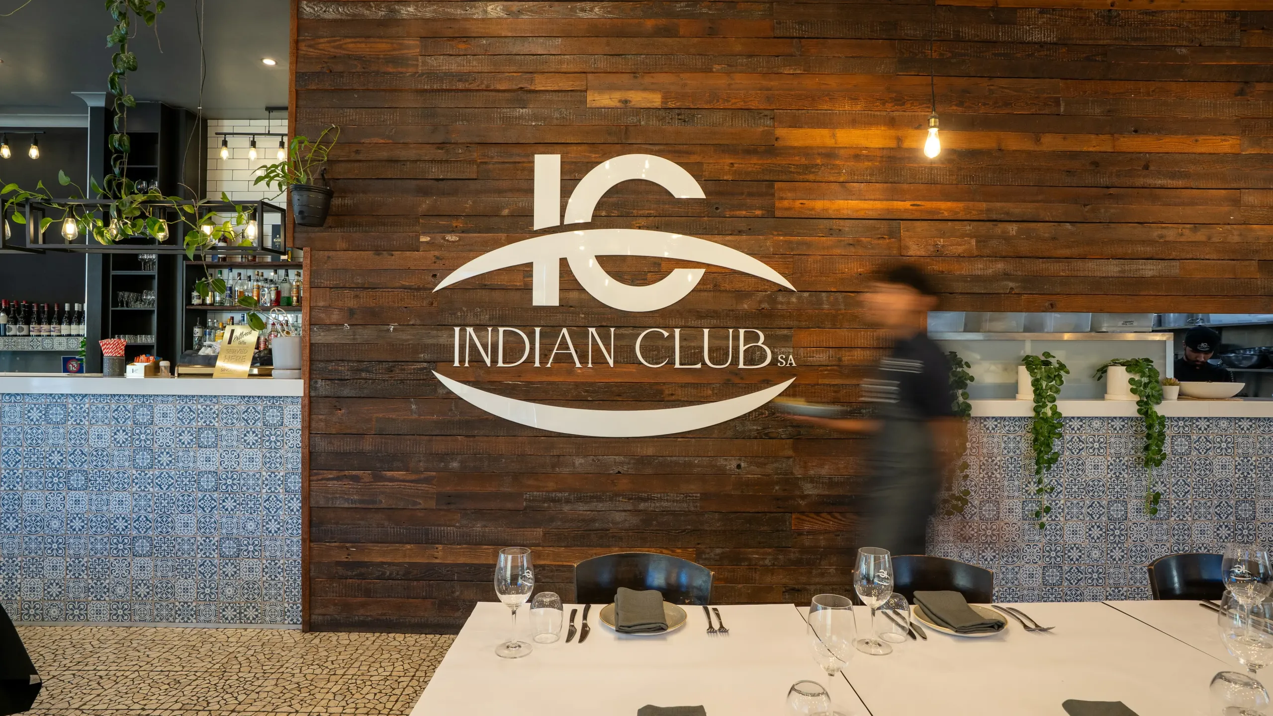 Waiter with food walking past an Indian Logo SA logo on the wall.
