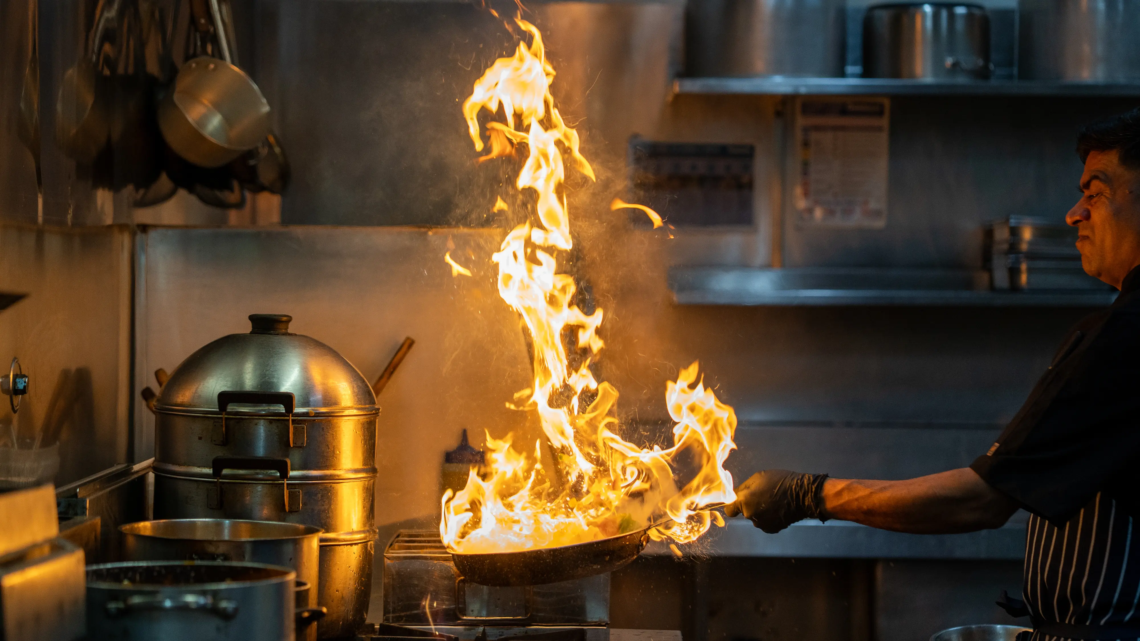 Chef tossing pan with high-reaching flames.