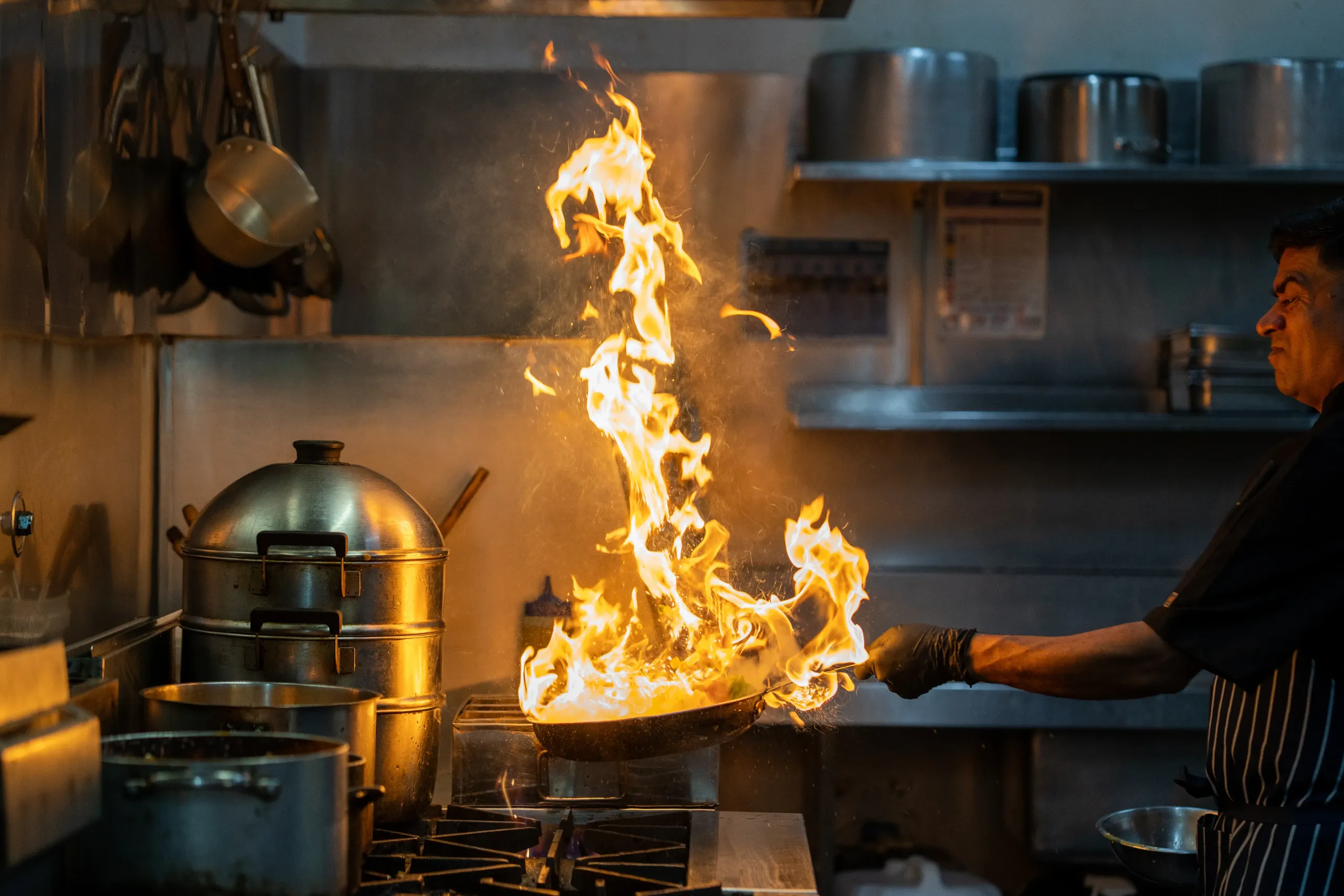 Chef tossing pan with high-reaching flames.